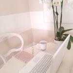 Scrivania bianca con PC, agenda rosa e orchidea bianca, spazio creativo per comunicazione e PR